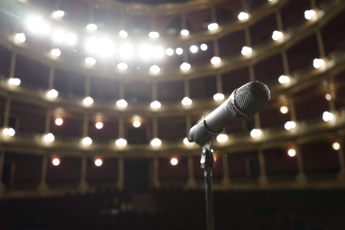 Microphone on an empty theatre stage under house lights, illustrating the 2026 BIGHIT MUSIC Global Audition open to boys born in 2008 or later
